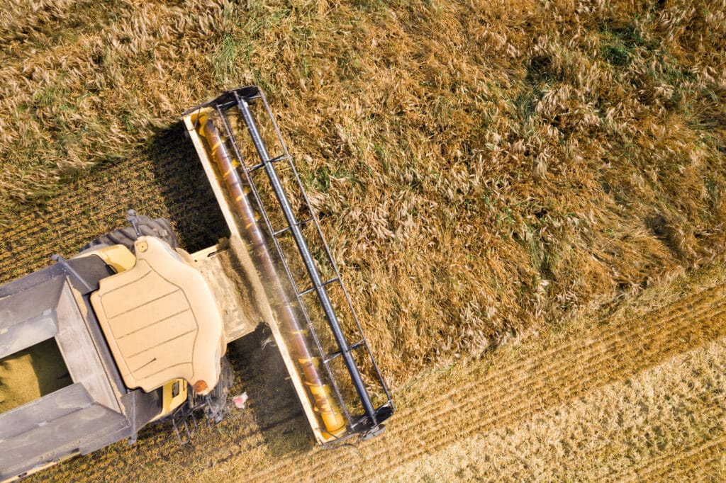 Aerial close-up of a combine harvester cutting through a large ripe wheat field