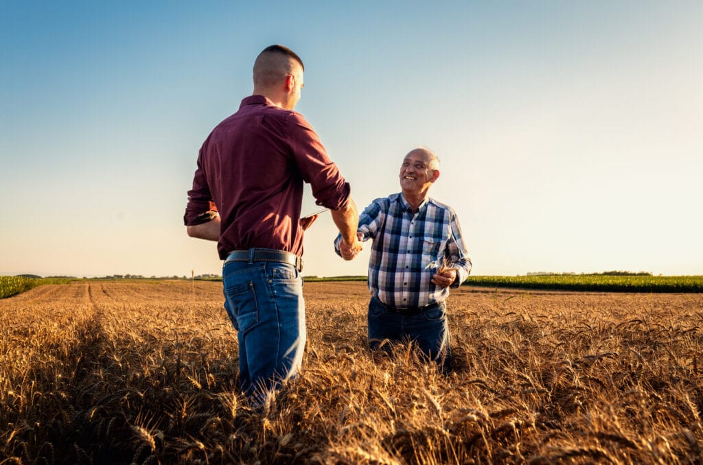 Two farmers shaking hands in a wheat field at sunset